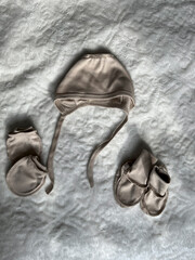 A beige set of accessories for a newborn baby lies neatly on a light blanket. A cap, socks, and...