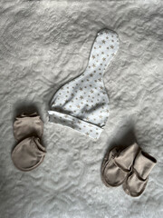 A stylish set of accessories for a newborn baby lies neatly on a light blanket. A hat, socks, and scratches. Top view