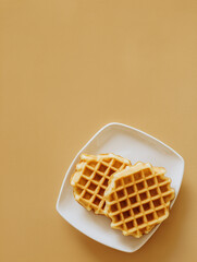 Two round waffles on a white plate with golden brown color on beige background, delicious breakfast treat