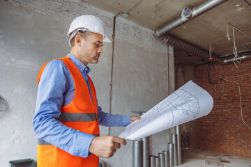 Construction manager reviewing plans in a partially finished building with exposed walls and pipes