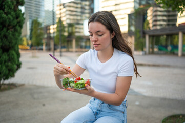 Young woman enjoying a fresh salad with chopsticks in urban park
