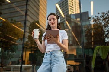 Young woman using tablet and drinking coffee outdoors in urban setting