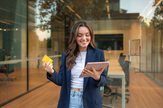 Smiling businesswoman using tablet and credit card for online shopping outside office