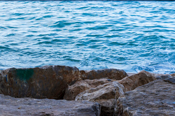 Rocky shoreline beside calm turquoise sea, highlighting natural textures and colors. Ideal for illustrating nature, relaxation, and coastal scenery.