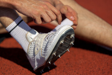 The athlete secures the laces on their spiked running shoes while standing on the track surface....