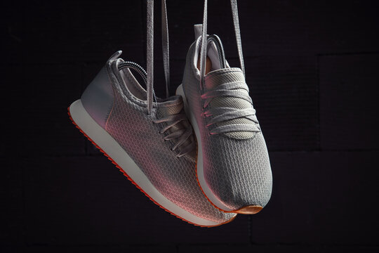 Hanging Gray Mesh Sneakers with Orange Soles on Dark Background