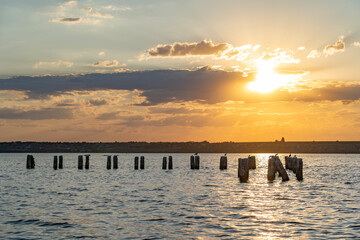 Evening sunlight spreads across the horizon as seagulls rest on old wooden pier remnants in the...