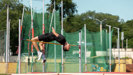Athlete executing high jump at outdoor track and field event on a sunny day. Concept of jump technique, body coordination, aerial control in pole vault
