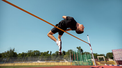 Athlete executes high jump at an outdoor sports venue beneath a blue sky. Concept of slow motion sports sequence, athletics for educational use, motion analysis