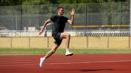 Youthful male runner dashing along an outdoor track beneath a sunny sky. Concept of step technique...