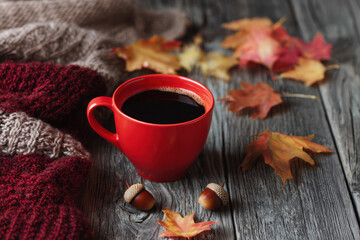 Autumn background with a red coffee mug, autumn leaves, and a knitted blanket on a wooden table