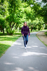 A visually impaired woman walking in the park with white cane