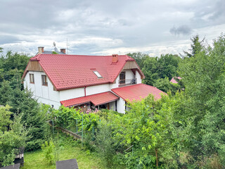 A charming countryside house with a red tiled roof is surrounded by lush greenery