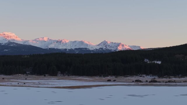 Beautiful glowing snowy mountain peaks above distant forests at Laguna La Zeta, Esquel, Province of Chubut, Argentina.