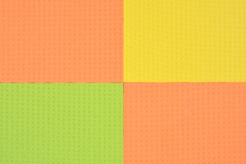 A four-part mosaic of kitchen sponge material in yellow, orange, and green colors.