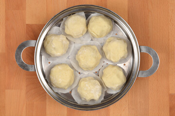 Raw potato dough dumplings placed on parchment paper inside a metal steamer pot, set on a wooden surface