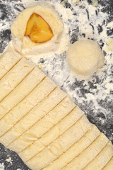 The preparation process of potato dough and peach dumplings, with sliced dough and several developing dumplings dusted with flour on a dark surface