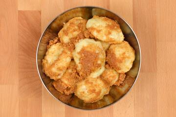 A bowl full of cooked potato dumplings topped with toasted breadcrumbs, set on a wooden surface