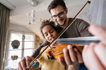 Music is so much fun. Young father teaching his little daughter to play violin and smiling.