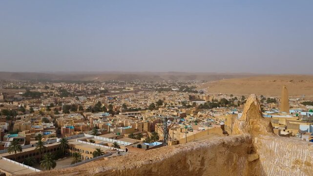 Panoramic view of Gharda&iuml;a, Algeria, a Saharan oasis town with mud-brick houses, swaying palms, and desert hills, showcasing the timeless charm of North African tradition