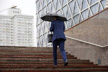 Heavy rain in city, man in business suit walking up with umbrella the steps on city buildings...