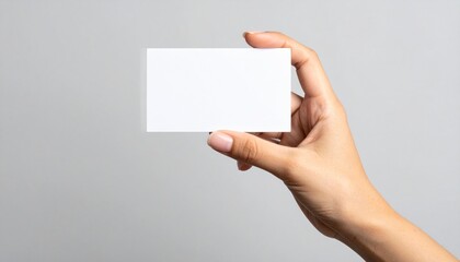 Fototapeta premium Mano de mujer sosteniendo una tarjeta blanca sobre fondo gris