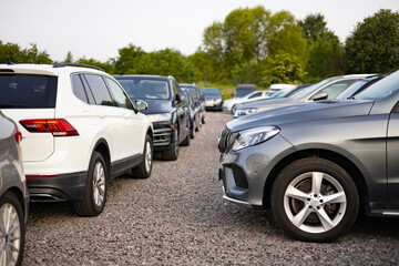 A row of cars of different models parked outdoors on a gravel surface, ready for sale. The vehicles...