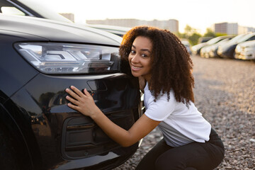 A smiling woman embraces a new black car, likely at a car dealership or lot, excited about her...