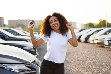An ecstatic woman celebrates after buying a new car, holding up the keys with joy in a dealership.