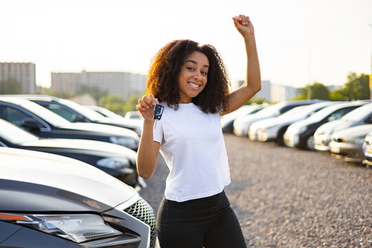A happy woman celebrates her new car purchase, holding up the keys with excitement in a dealership.