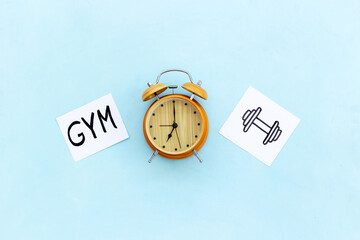 Retro alarm clock with paper cards with hand drawing of gym activities, top view. Time management...