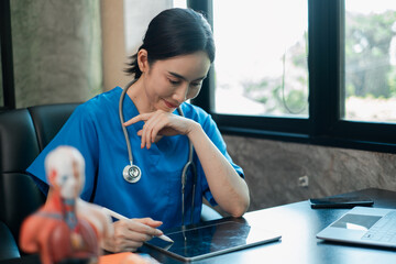A healthcare worker in blue scrubs uses a tablet in a contemporary office setting, emphasizing...