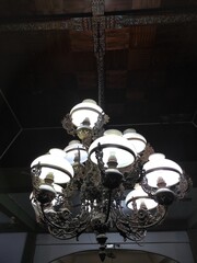 A detailed, ornate chandelier hangs from a dark, patterned ceiling, showcasing vintage elegance and decorative interior design elements.