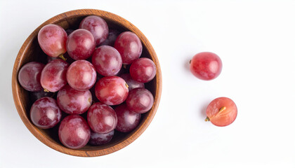 Obraz premium a wooden bowl is filled with numerous red purple fruits, occupying the left side of the scene