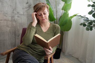 Woman reading a book and touching her head while sitting on a chair