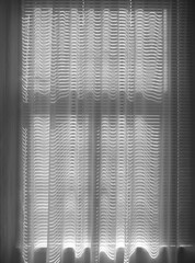 Sunlight filters through sheer curtains and blinds, casting wavy light patterns in a soft,...