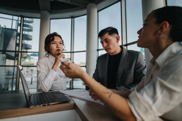 A group of three business professionals engaged in a thoughtful meeting inside a contemporary...