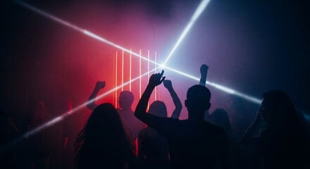 Silhouettes of people dancing energetically amidst vibrant laser lights and atmospheric smoke at a lively night event.