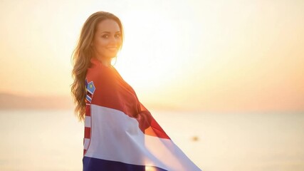 Beautiful young woman wrapped in a Croatian flag on the beach. Portrait of a patriotic female fan smiling at sunset with national pride. - Powered by Adobe
