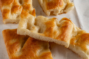 Soft pieces of golden, inviting Ligurian focaccia rest on a slightly oiled wrapping paper, ready to be enjoyed.