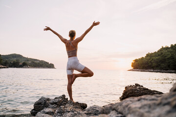 Woman practicing yoga at seaside at sunset or sunrise. Holistic Health and Mental Well-Being.