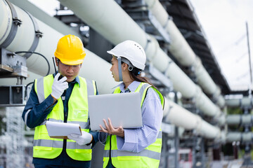 Engineer working at power substation with high voltage infrastructure performing inspection and...