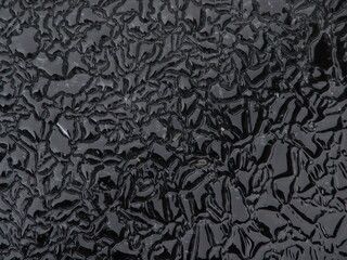 Close-up of a textured black surface with intricate, irregular patterns resembling cracks or veins,...
