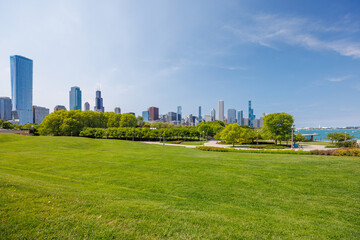 Obraz premium Sunny view of downtown Chicago with iconic skyscrapers rising above a lush green park meadow