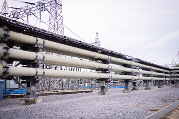 High voltage power substation infrastructure with large insulated pipes and metal framework under cloudy sky in industrial area