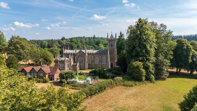 Aerial view of a church nestled amidst lush greenery, with the quaint village buildings adding a touch of rustic charm against the blue sky., Guildford, England, United Kingdom.