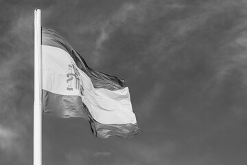 National flag of Spain flying in the wind; yellow and red national flag in black and white on cloudy sky background