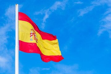 National flag of Spain flying in the wind; red and yellow national flag on blue sky background