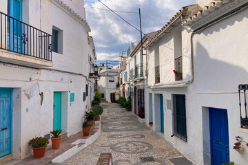Fototapeta premium FRIGILIANA, SPAIN - MAY 10, 2025: A peaceful walk through the charming narrow streets, surrounded by whitewashed houses and colorful flowers in Frigiliana, Spain
