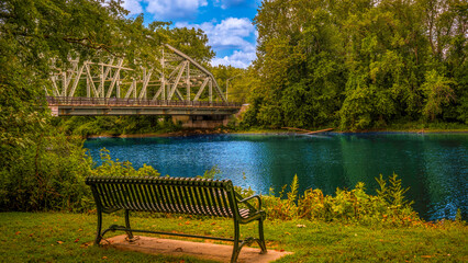 Tranquil summer landscape with an empty bench on the riverbank of the Housatonic River in New Milford, Connecticut with the view of the New Milford Veteran’s Memorial Bridge